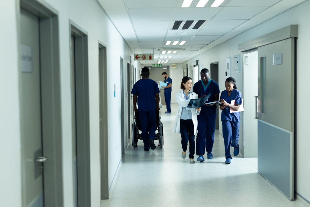 Diverse female doctor and healthcare workers discussing and walking in hospital corridor, copy space.